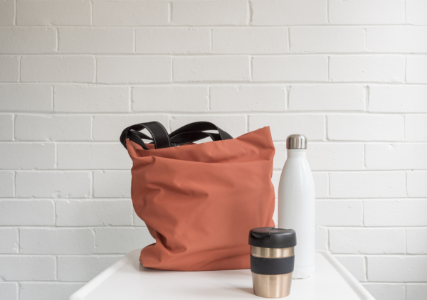 Reusable coffee cup, insulated drink bottle and shopping tote bag on white table against brick wall with copy space