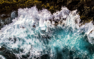 Aerial view to ocean waves. Blue water background - top vertical view of coastline and big power waves on the rocks - splash and dangerous concept for nature outdoor beauty