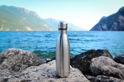 A metal reusable water bottle near a lake